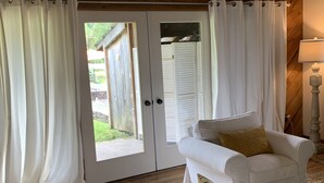 Una habitación con techo de madera, un sofá blanco con cojines, un sillón blanco y una puerta que da a un área exterior.