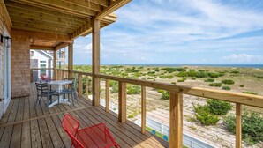 A wooden deck with a table and chairs, overlooking a beach with sparse vegetation. - Fantastic Oceanfront Modern Coastal Home w/ Saltwater Pool - Simply the best! (Salvo)