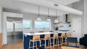 A modern kitchen with a large island, stainless steel appliances, wooden bar stools, and pendant lighting. - Fantastic Oceanfront Modern Coastal Home w/ Saltwater Pool - Simply the best! (Salvo)