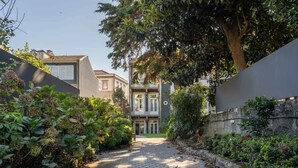 Un étroit sentier pavé de pierres menant à un bâtiment doté d’un balcon, entouré d’une végétation luxuriante et d’un mur de pierre.