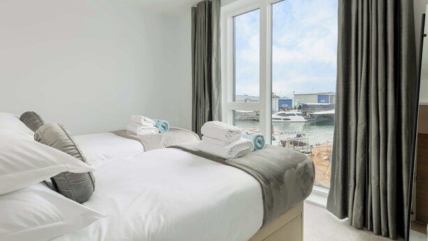 A hotel room with two beds, a large window with curtains, and a view of boats and docks. - Endless Summer - Spacious Living Space  Poole Quay (Poole)