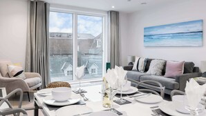 A modern living room with a dining area, large windows, and a view of buildings. - Endless Summer - Spacious Living Space  Poole Quay (Poole)