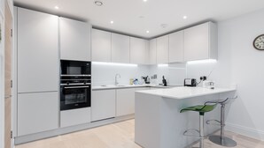 A modern kitchen with white cabinetry, a built-in oven, a sink, and a bar area with stools. - Endless Summer - Spacious Living Space  Poole Quay (Poole)