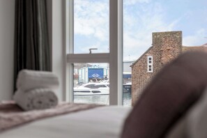 Une chambre avec une grande fenêtre donnant sur un port de plaisance et un bâtiment avec une enseigne bleue.