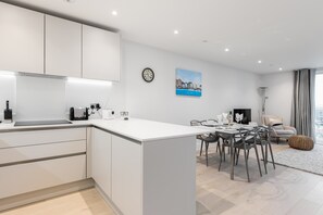 Une cuisine moderne avec des meubles blancs, un coin repas doté d’une table ronde et un tableau représentant un paysage urbain accroché au mur.