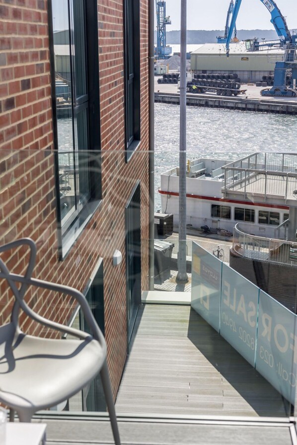 Un balcon donnant sur un quai et un bateau, un bâtiment en briques et une enseigne sur laquelle on peut lire « ROSE SALLE ».