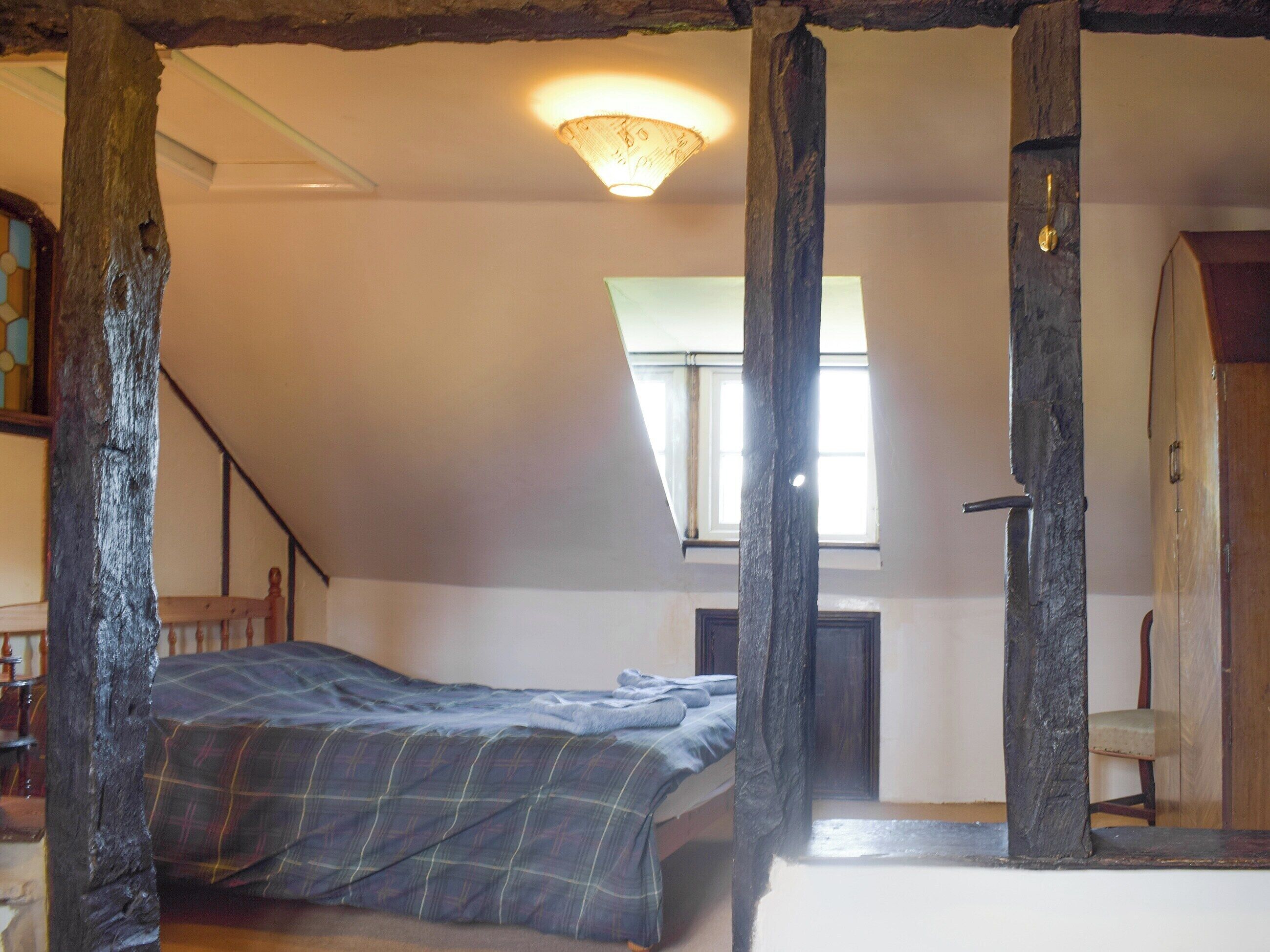 Une chambre à coucher comprenant un lit, une chaise en bois, une armoire en bois, une fenêtre et un plafond en pente.
