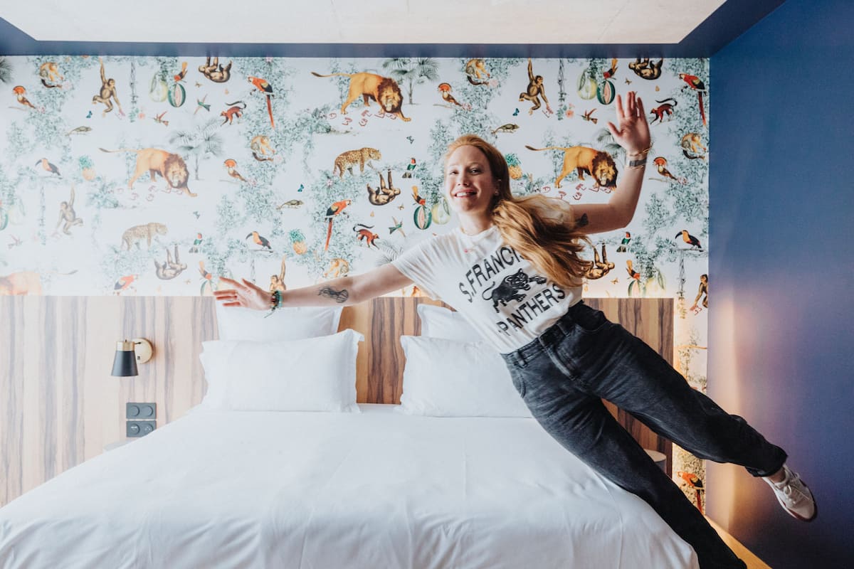A room with a bed, a wall with animal prints, and a person jumping.