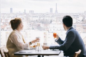 Una pareja cenando en una mesa con vista a un paisaje urbano, incluyendo una torre alta.