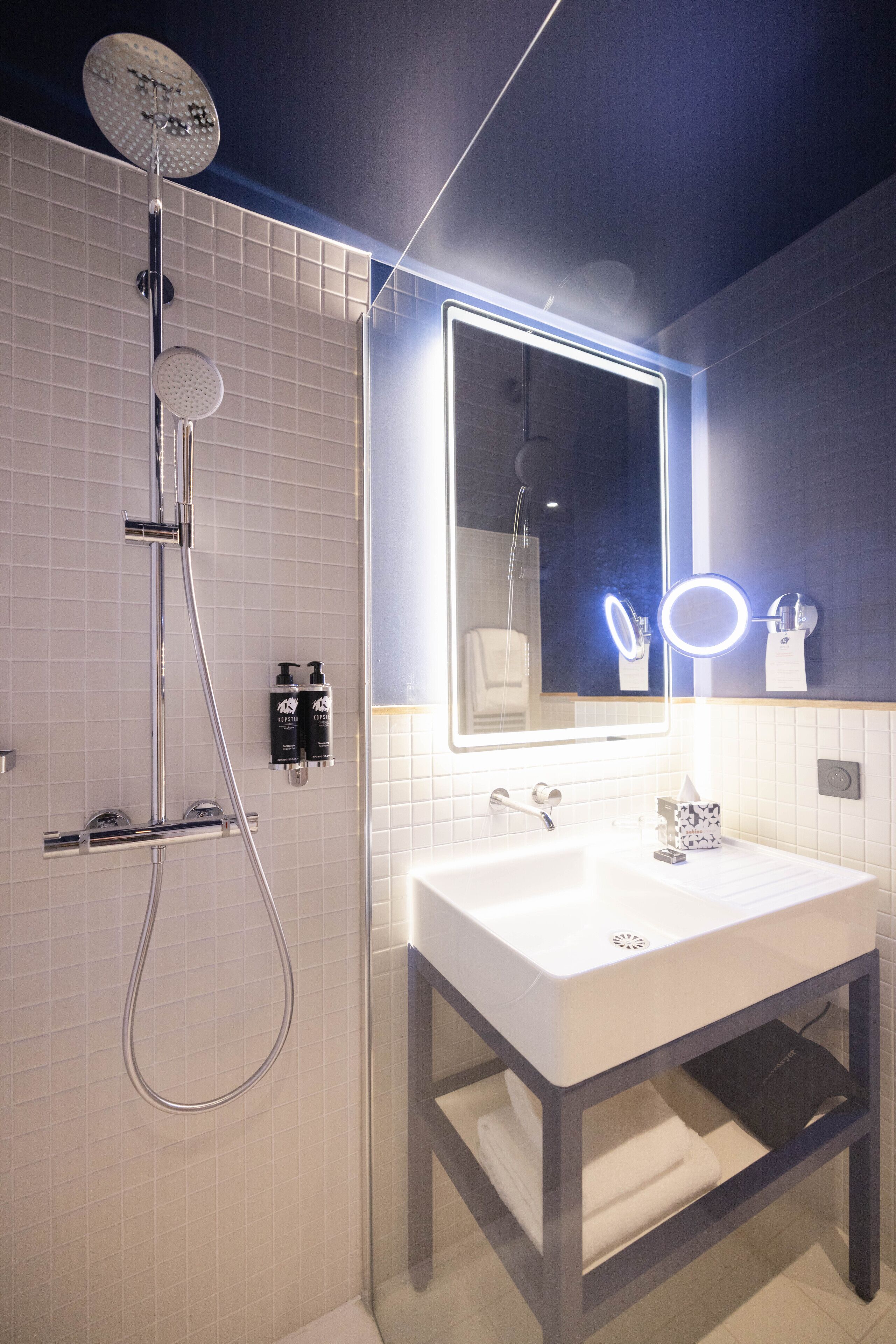 A modern bathroom with a white sink, a handheld showerhead, and a mirror with illuminated lights.