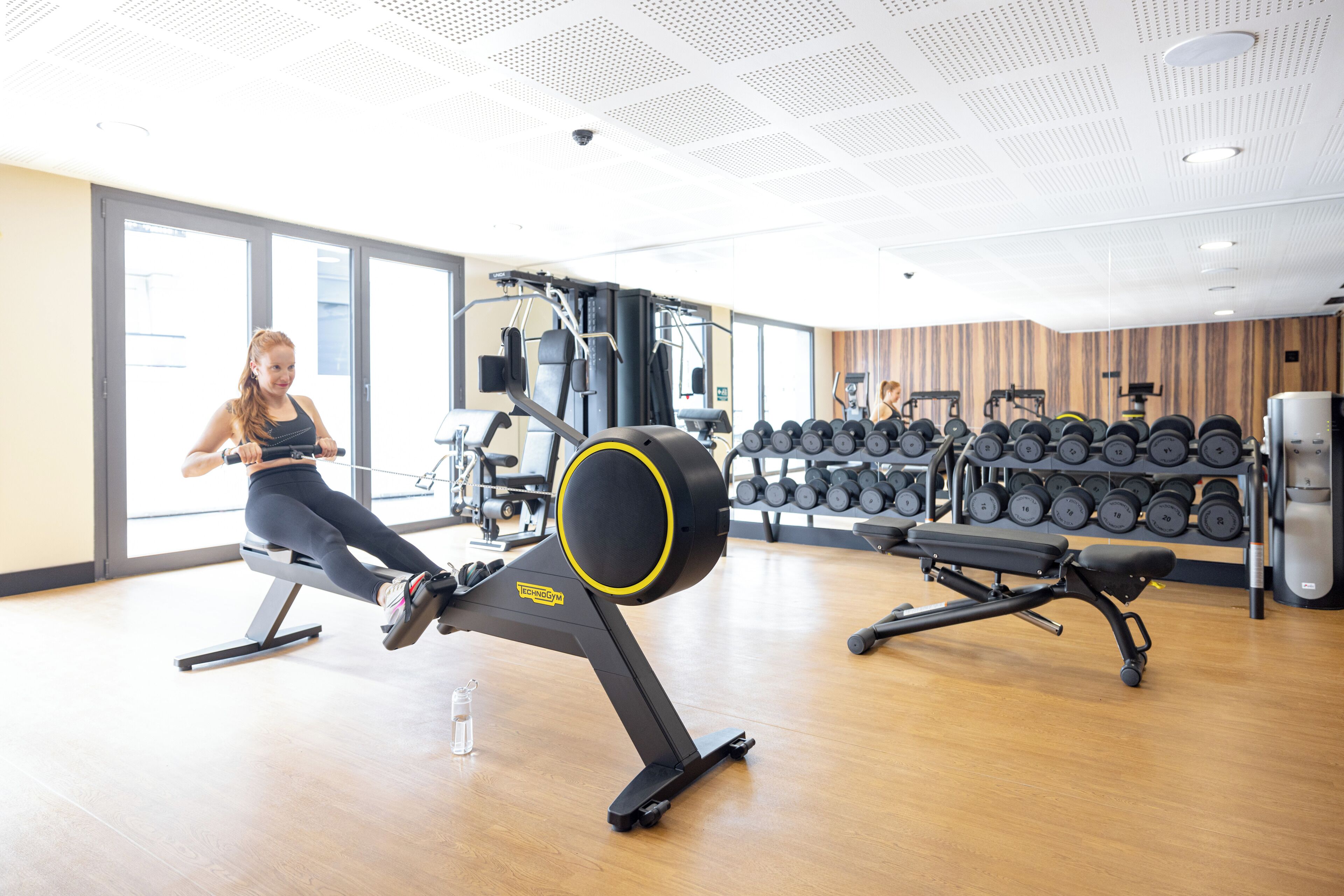 Une salle de sport équipée de machines de cardio, de supports pour les poids et dotée d’un plancher en bois.
