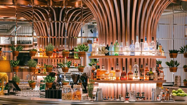 A bar area with a curved wooden ceiling, bar stools, and a variety of bottles and glasses on the counter. - KOPSTER Hotel Residence Paris Colombes (Colombes)