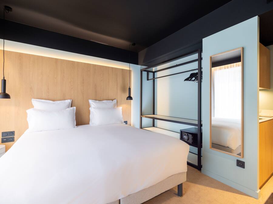 Une chambre d’hôtel moderne avec un grand lit, des tables de chevet, une armoire et un miroir intégré.