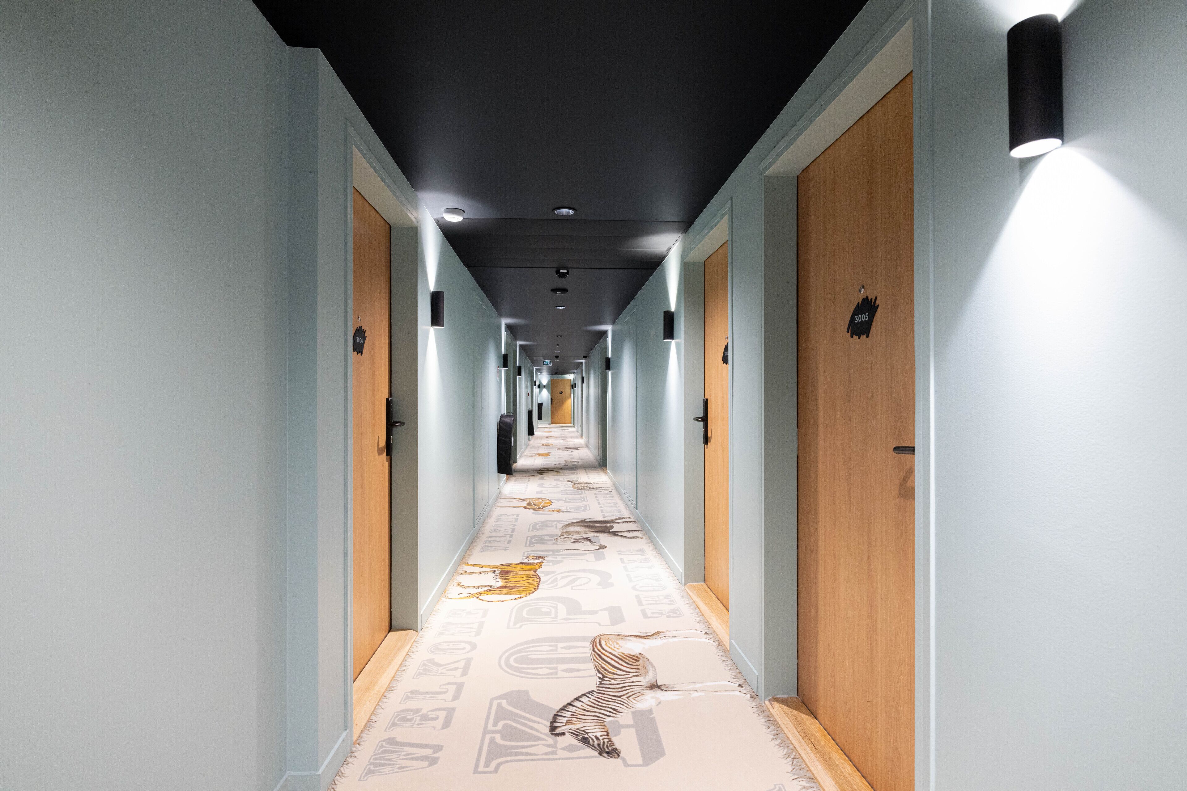 Un pasillo largo de hotel con puertas de madera y una alfombra estampada con motivos animales.