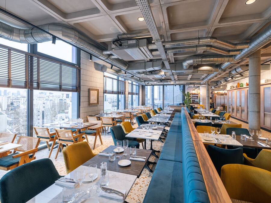 A modern restaurant with a long counter, multiple dining tables, and chairs.