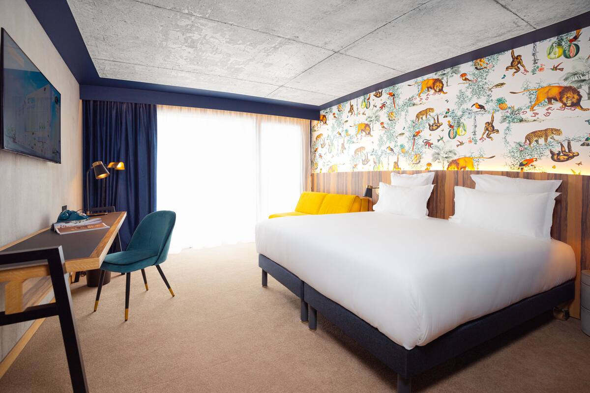 A hotel room with a bed, a desk, a chair, and a large window with curtains.