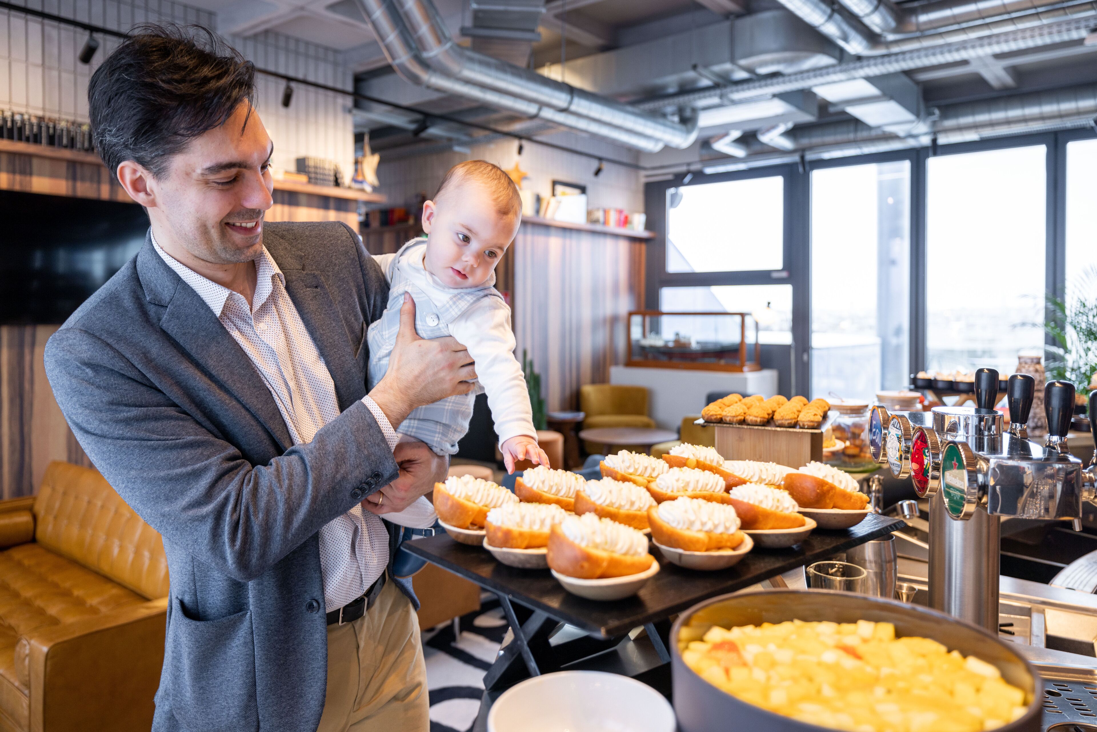 Ein Mann hält ein Baby in einer modernen Küche mit einer Kaffeebar und Gebäck.