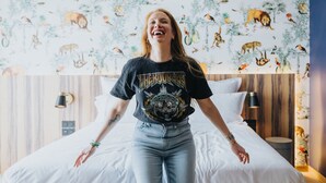 A person standing in a bedroom with a bed, a wooden headboard, and a wall with animal prints. - KOPSTER Hotel Residence Paris Colombes (Colombes)