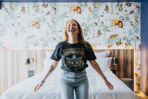 Uma pessoa em um quarto com uma cama e cabeceira de madeira, e parede com estampas de animais.