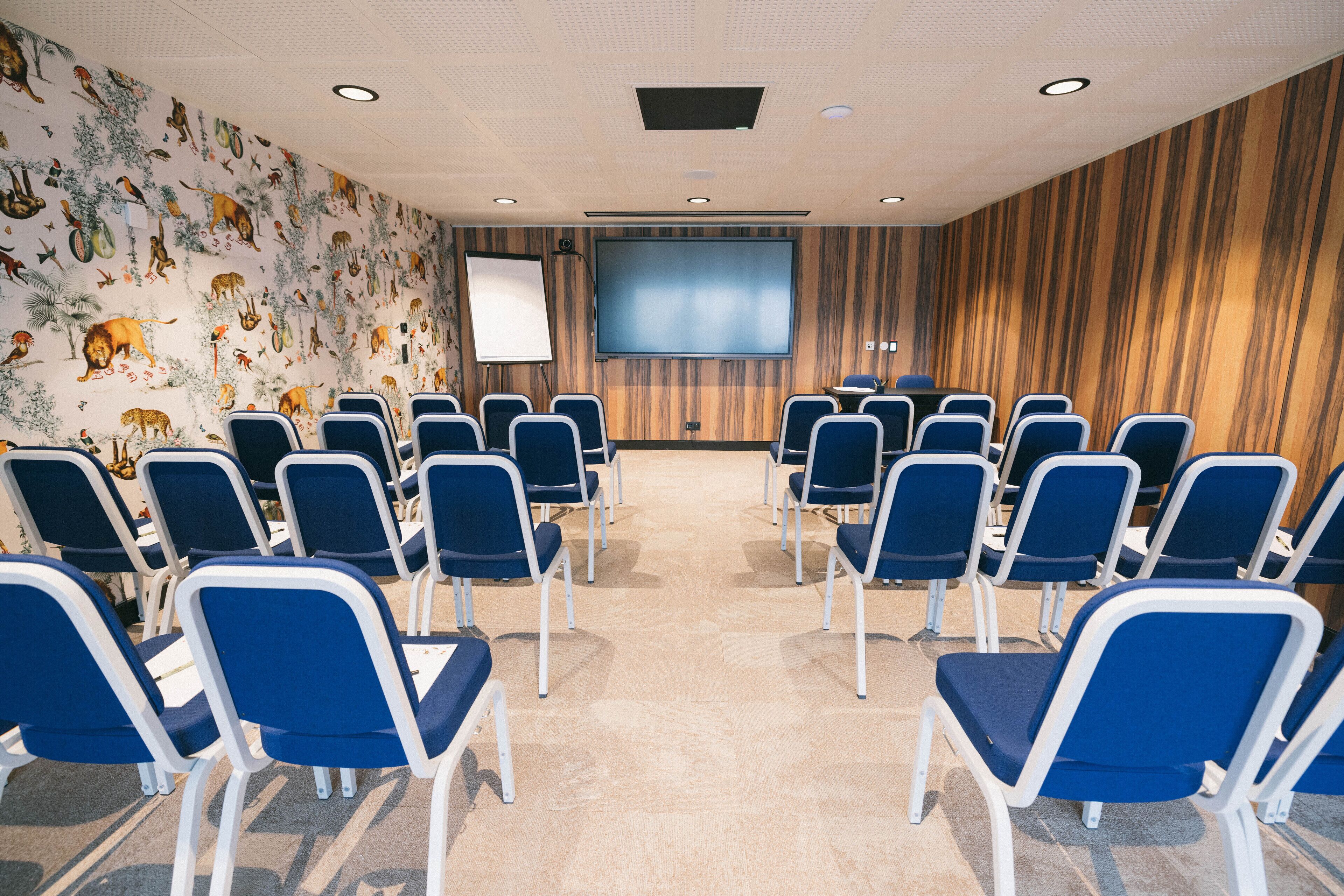 Un salón de conferencias con filas de sillas azules, una pantalla grande y una pizarra.