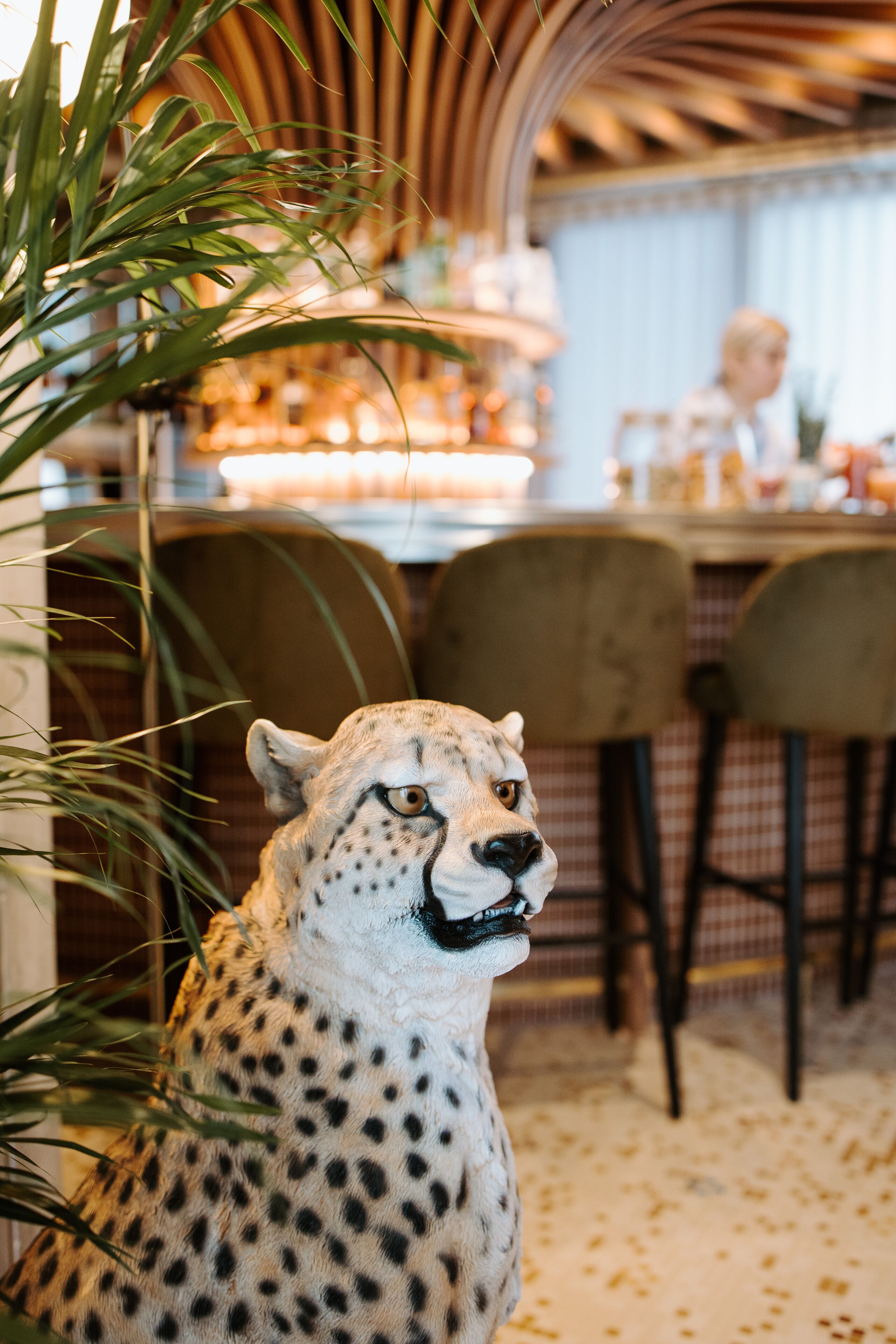 Una estatua de un guepardo en un restaurante, con una zona de bar y sillas al fondo.