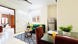 Una sala de estar moderna con un sofá verde, una mesa de comedor con sillas, una mesita auxiliar con un vaso de jugo de naranja y un refrigerador.