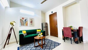 Una sala de estar con un sofá verde, una mesita redonda con un florero, una lámpara de trípode y arte abstracto en la pared.