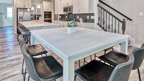 A modern kitchen with white cabinets, a central island, and a dining area with chairs. - Bayside * 5BR Luxury Home (Selbyville)