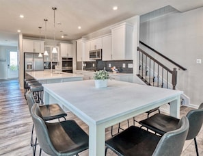 A modern kitchen with white cabinets, a central island, and a dining area with chairs.