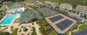 An aerial view of a resort with a swimming pool, tennis courts, and a covered pavilion.