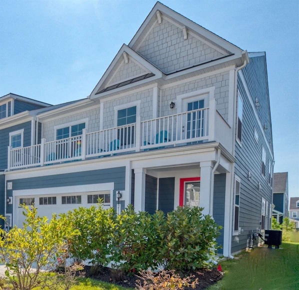 A two-story residential building with a front garage, a balcony on the second floor, and a well-maintained front yard.