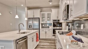 A modern kitchen with white cabinetry, stainless steel appliances, and a wooden floor. - Bayside * 5BR Luxury Home (Selbyville)
