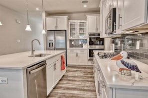 A modern kitchen with white cabinetry, stainless steel appliances, and a wooden floor.