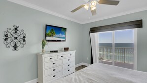 Un dormitorio con cama, cómoda, televisor y vista al océano.