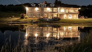 Ein großes, mehrstöckiges Haus mit einem Teich davor, umgeben von Gras und Bäumen.