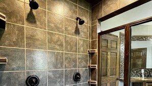 Ein modernes Badezimmer mit einer Holzbank, einer Dusche mit Glastür und Blick auf die Küche durch die Glastür.