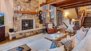 A cozy living room with a stone fireplace, leather sofa, and a staircase leading to an upper level.