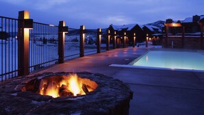 A pool area with a fire pit, a fence, and buildings in the background.