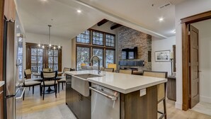 Une cuisine moderne dotée d’un grand îlot central, d’un coin repas avec des chaises et d’un mur d’accent en pierre.