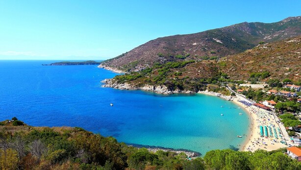 Un paysage côtier avec une plage, une mer bleue et limpide, et un relief montagneux.