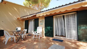 Une terrasse avec une table et des chaises, un sol carrelé et un bâtiment aux volets verts et au toit en tuiles.