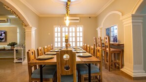 Une salle à manger avec une longue table en bois dressée pour le repas, entourée de chaises en bois dotées d’assises rembourrées.