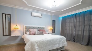 Une chambre à coucher avec un grand lit, deux lampes de chevet, un luminaire au plafond et une fenêtre avec des rideaux.