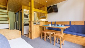 Une pièce de taille modeste, avec un bureau en bois, un banc et un téléviseur fixé au mur.