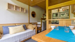 Une pièce confortable avec un plafond en bois, un lit avec des oreillers, une petite table avec des verres et une kitchenette équipée d’appareils électroménagers.