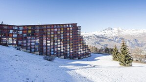 Um edifício moderno com várias varandas, com montanhas nevadas ao fundo.
