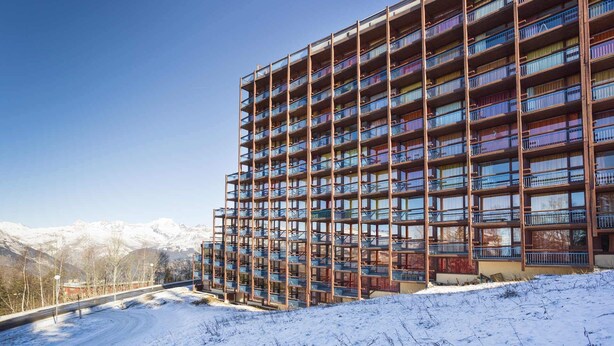 Hotel de vários andares com varandas, com uma paisagem de montanhas nevadas ao fundo.