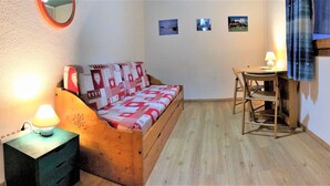 Une petite pièce agréable et chaleureuse, avec un lit en bois, un bureau et une chaise. Les murs sont ornés de tableaux et il y a un miroir.