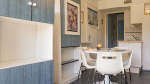 Una cocina moderna con armarios blancos, una mesa de comedor con sillas blancas y una pequeña isla con un lavamanos.
