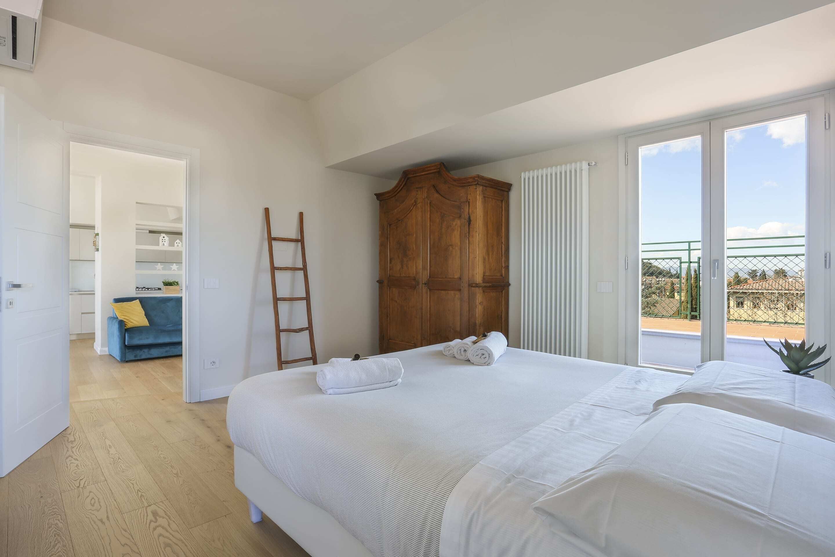 A bedroom with a large bed, a wooden wardrobe, and a view of a tennis court through the sliding glass door.